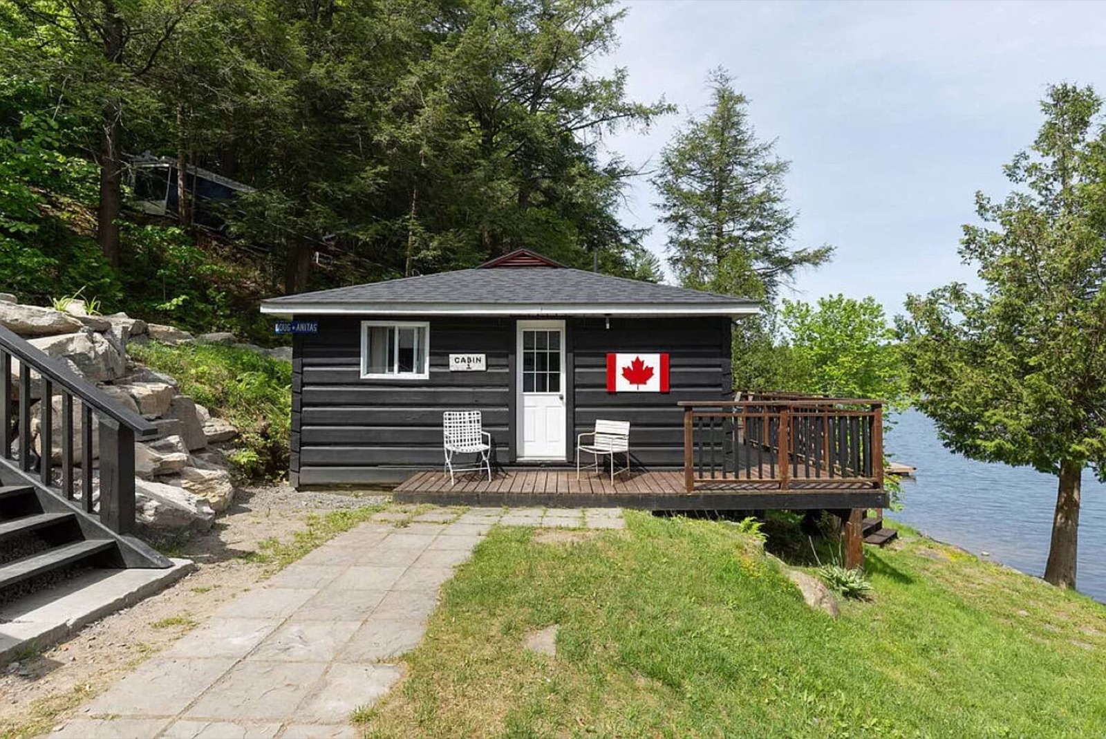 A black cabin with a Canadian flag beside the lake